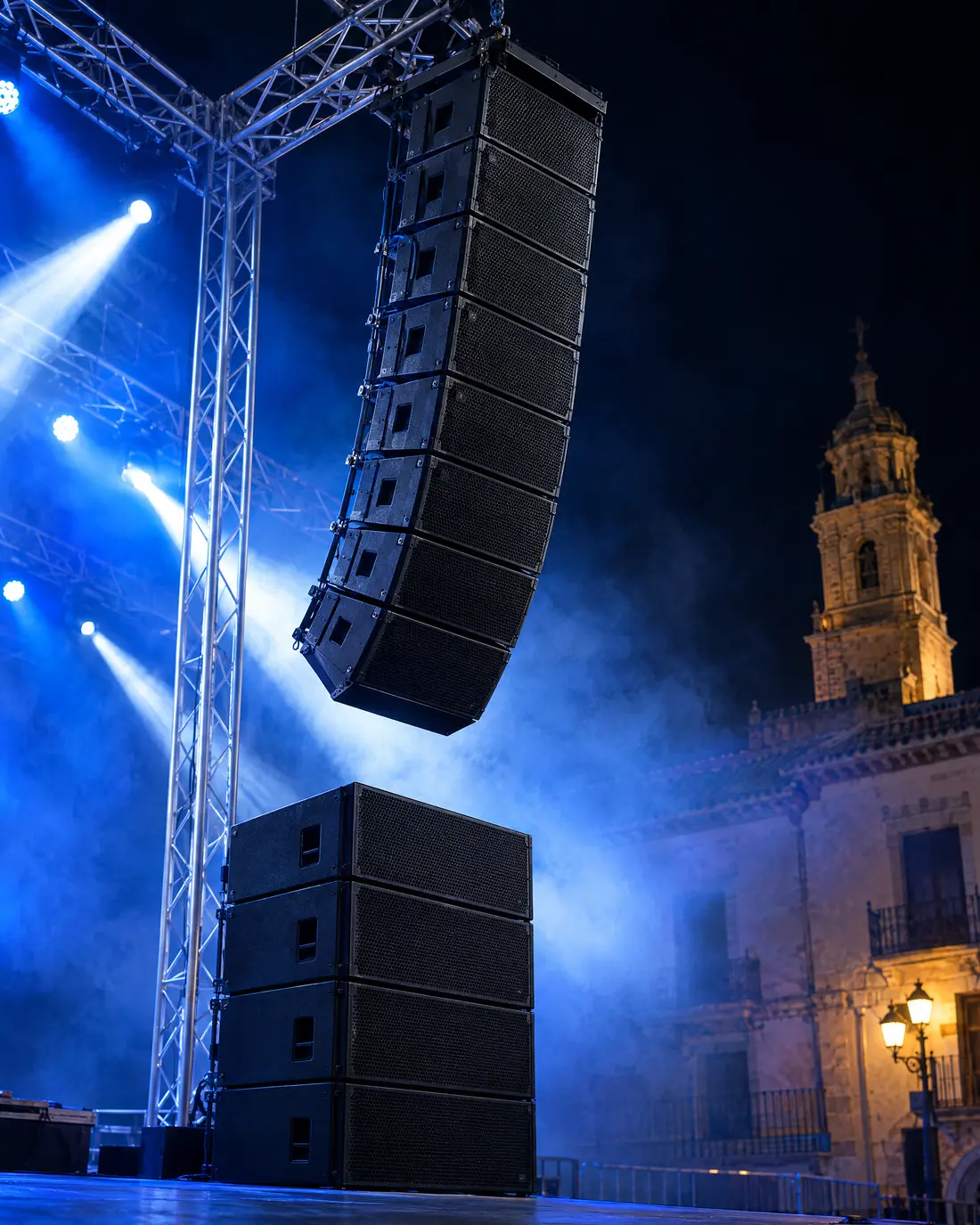 Line array colgado de una torre de truss en una plaza, con luz azul y humo